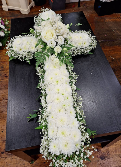 Cross - A timeless cross-shaped tribute arranged in elegant white tones with delicate foliage and soft detailing throughout. Designed to symbolise peace, faith, and everlasting love, this arrangement offers a heartfelt and dignified farewell in memory of a cherished loved one.